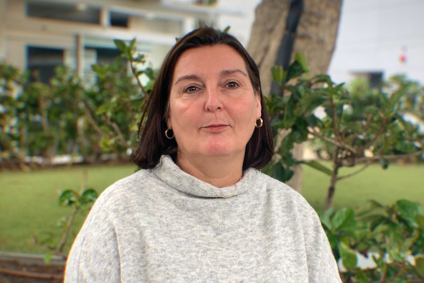 A woman with short brown hair stands in front of a garden bed