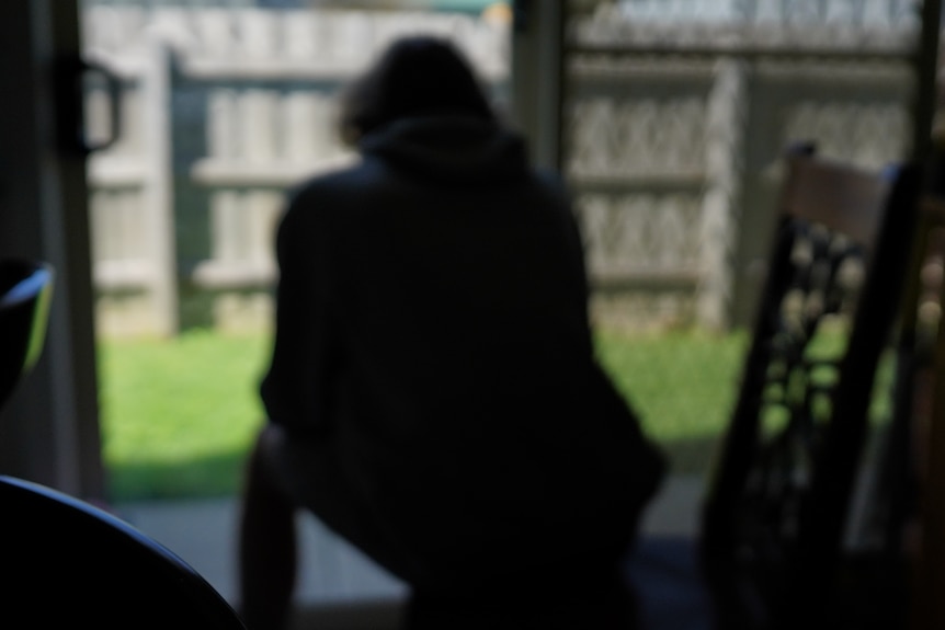 A boy is pictures from behind, sitting on a step, looking out into a yard.