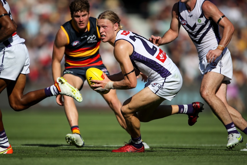 A man playing Australian rules football looks for options to dispose of the ball