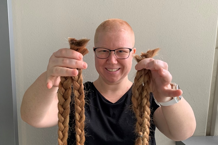 Rebecca Austin wearing glasses holds for pony tails of her own hair freshly cut from her own head.