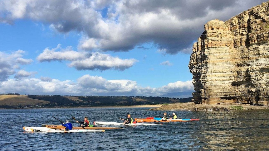 Craig Machen (front) and supporters kayak past Clifton in Tasmania's south east.