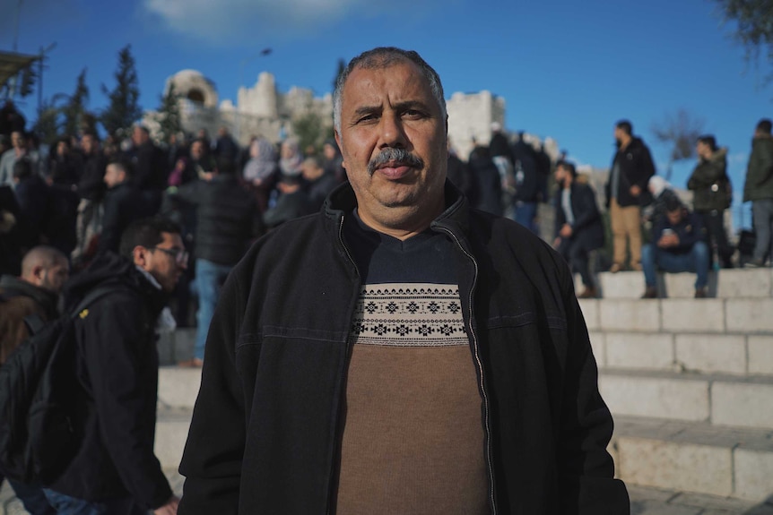 Mohammad Abu Al Hummus, 52, from East Jerusalem stares at the camera as people walk behind him.