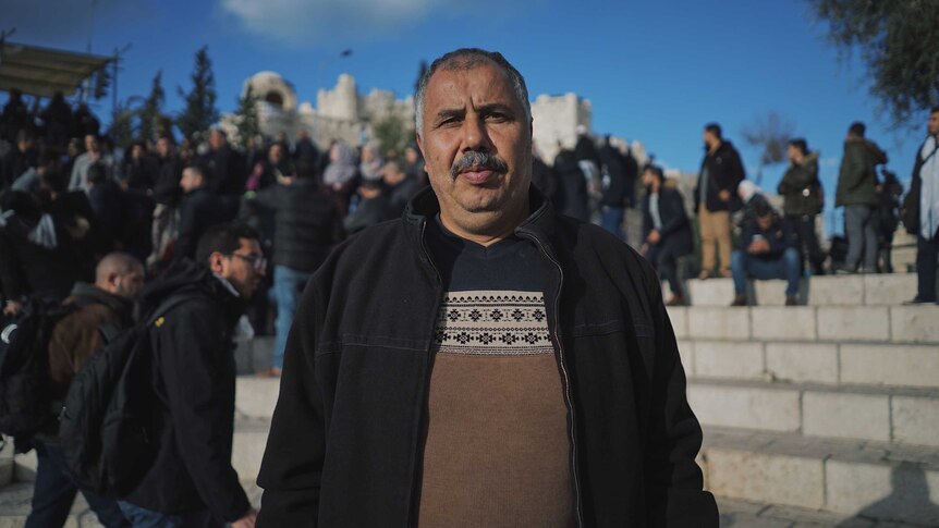 Mohammad Abu Al Hummus, 52, from East Jerusalem stares at the camera as people walk behind him.