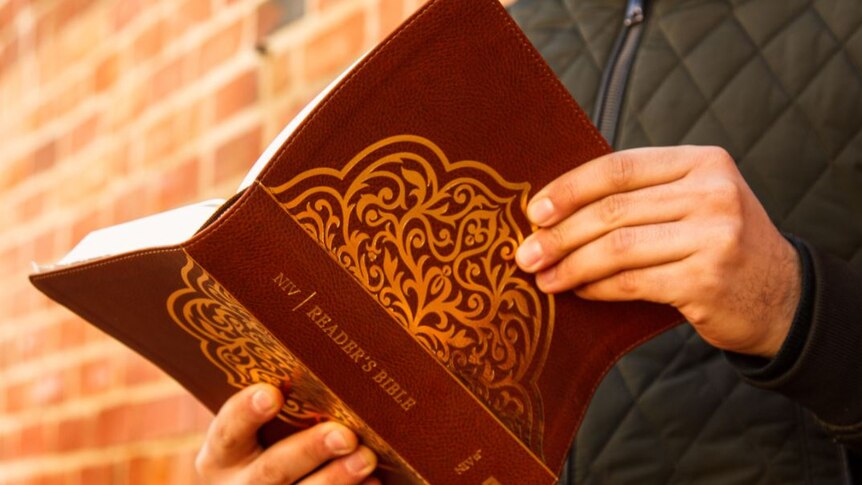 Short of the back of a bible being held by a man in a black jacket, no face showing