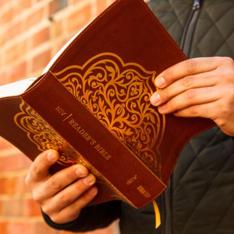 Short of the back of a bible being held by a man in a black jacket, no face showing