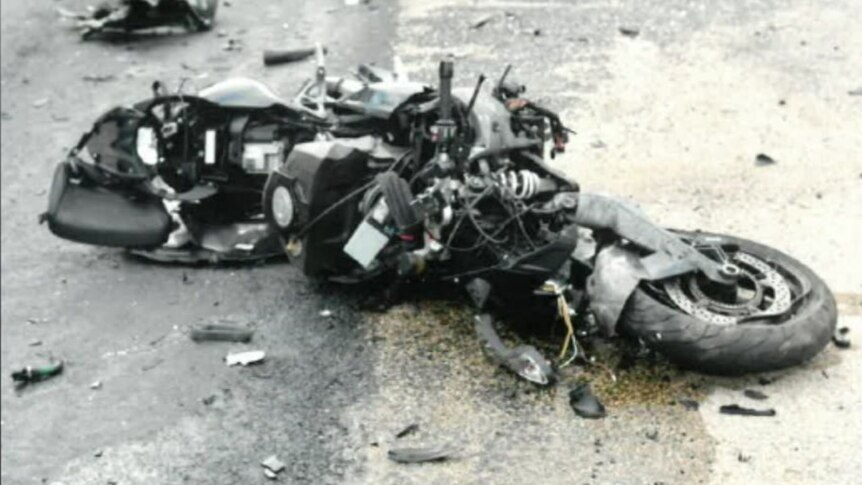 A smashed motorcycle lays in pieces on the road