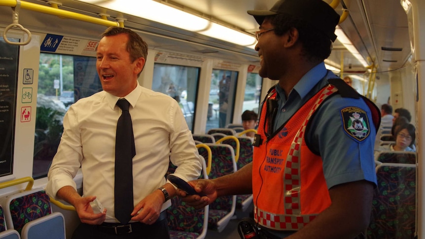 Mark McGowan in a train carriage joking with a train guard who asks to check his ticket