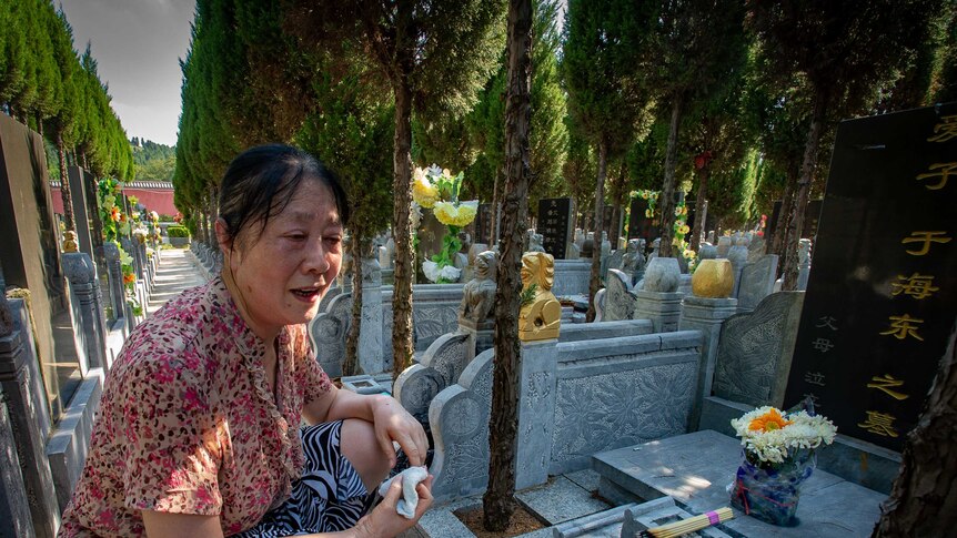 A woman sits by a gravesite adorned with flowers