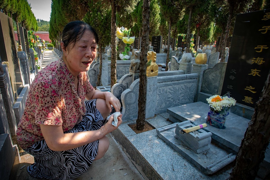 A woman sits by a gravesite adorned with flowers