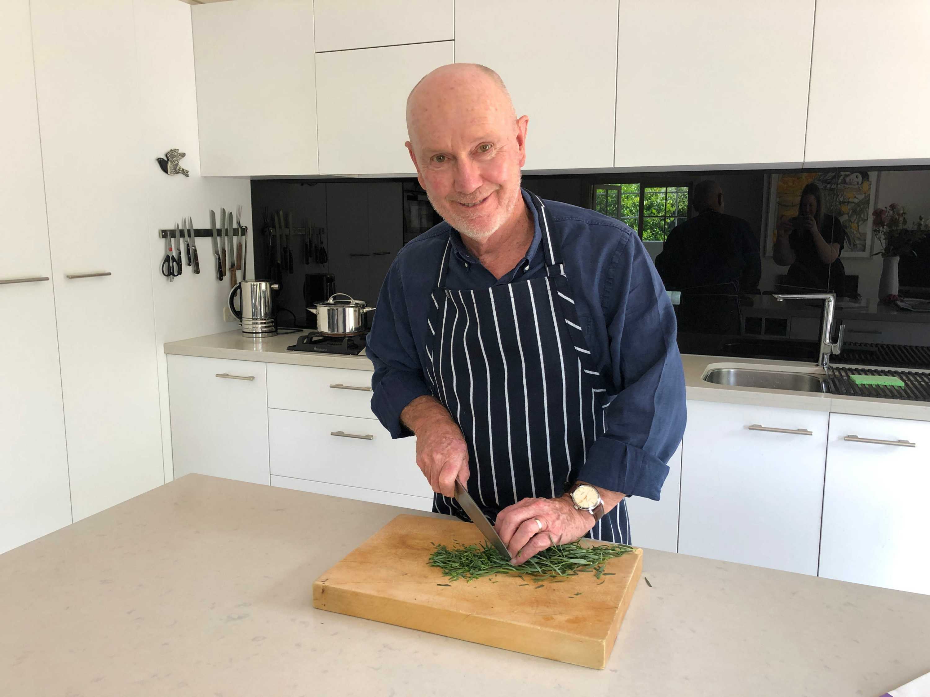 Rod Chandler wearing an apron, chopping herbs with a recipe book open in front of him.