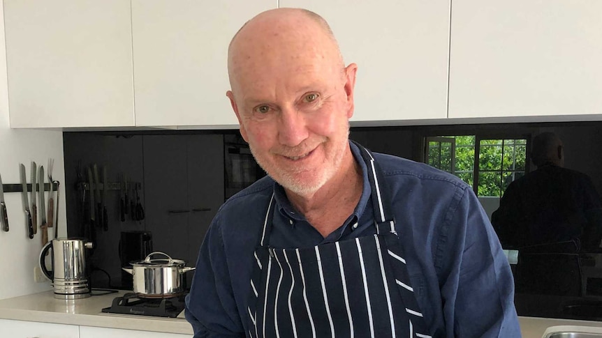 Rod Chandler wearing an apron, chopping herbs with a recipe book open in front of him.