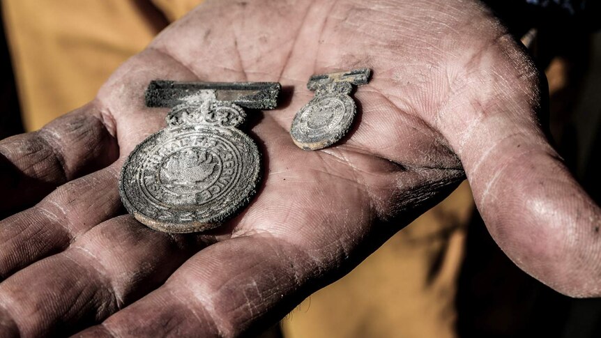 Open hand holding two charred medals with Rural Fire Service inscription barely visible.