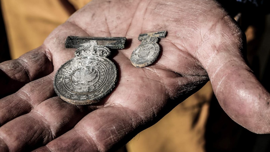 Open hand holding two charred medals with Rural Fire Service inscription barely visible.