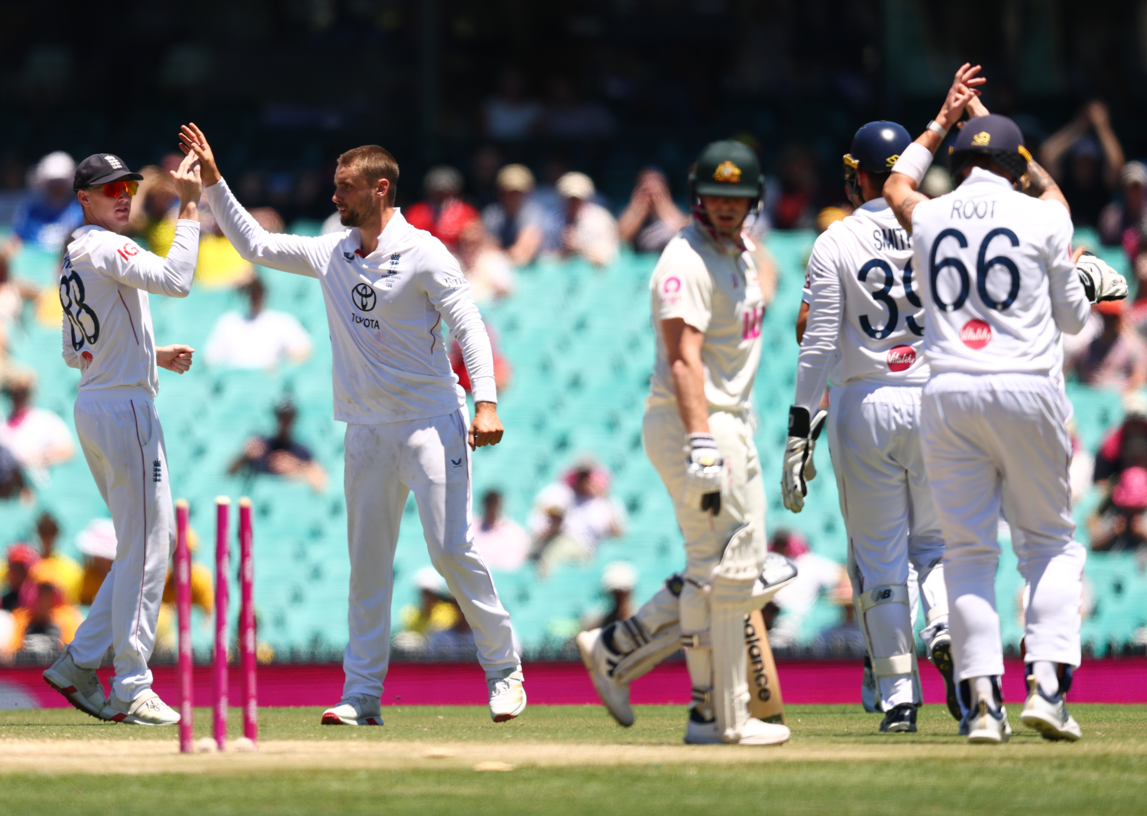 Um batedor de críquete olha para trás enquanto os tocos são retirados e outros jogadores comemoram