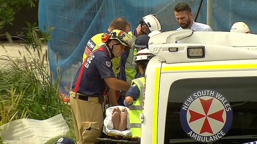 Emergency workers surround a man on a stretcher as he is being wheeled out to an ambulance.