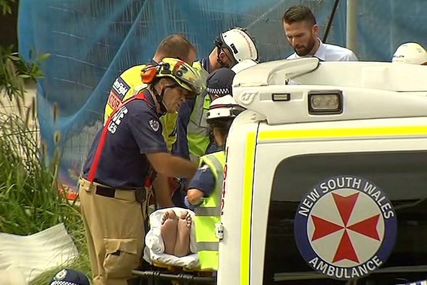 Emergency workers surround a man on a stretcher as he is being wheeled out to an ambulance.