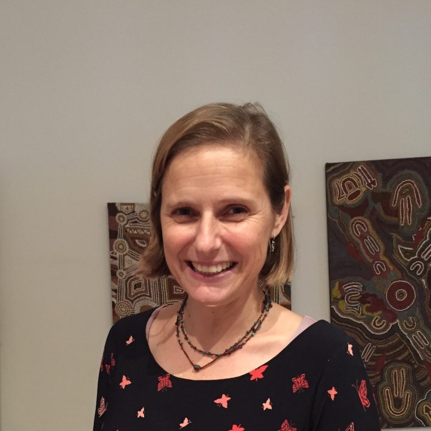 Kirsty Ruddock smiles with indigenous artwork on the wall behind her