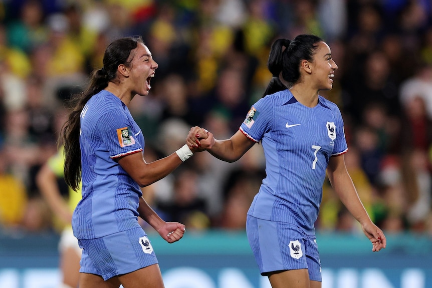 Two French footballers smile as they hold hands in celebration as their team gets a vital goal at the Women's World Cup.