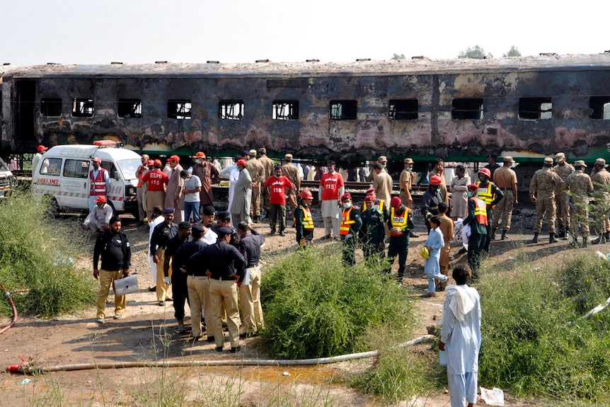 Dozens of Pakistani soldiers and officials stand ready to examine a train damaged by a fire.