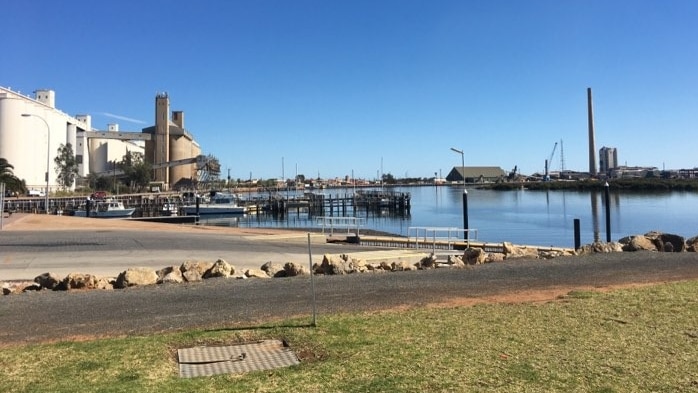 A blue river stretches out in the foreground, with silos and a large industrial plant on the bank