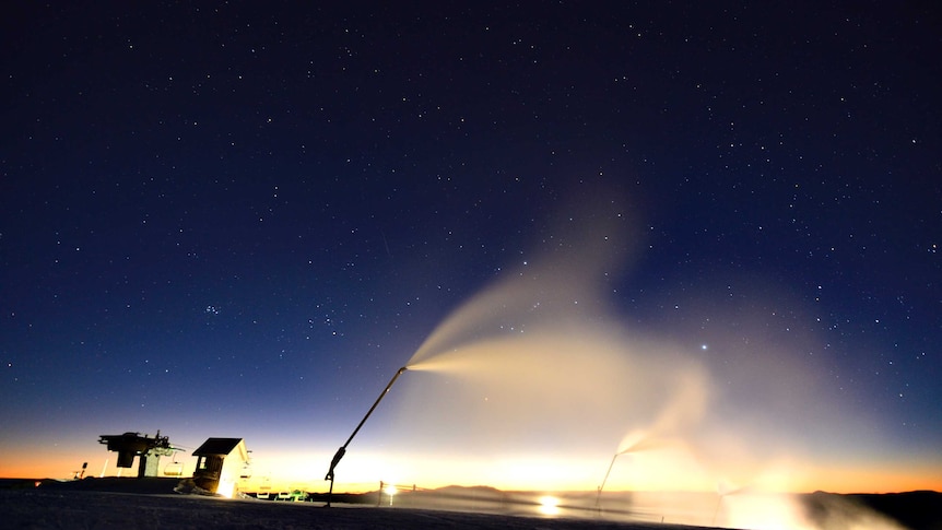 Dawn lights up a starry sky with snowmaking equipment spraying fresh snow in the foreground.