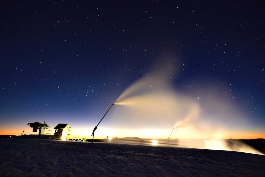 Dawn lights up a starry sky with snowmaking equipment spraying fresh snow in the foreground.