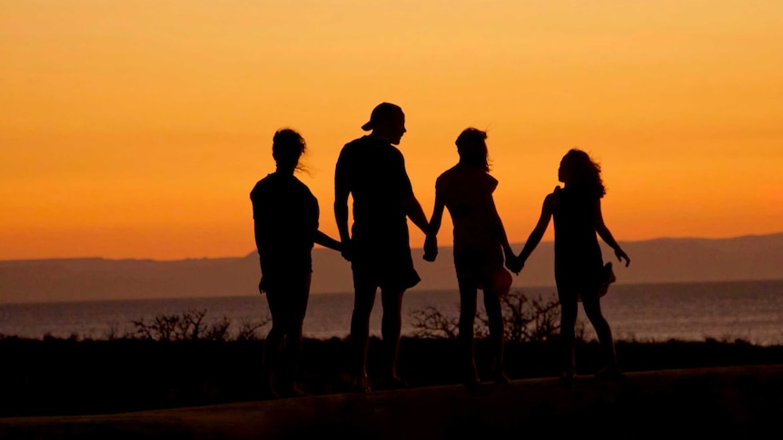 Silhouette shows four people holding hands while looking out to sea for a story about adult children and parents living together