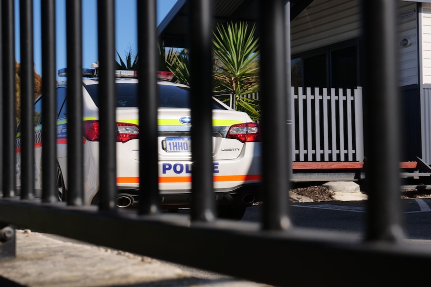 A police cruiser, as seen through the bars of a metal gate.