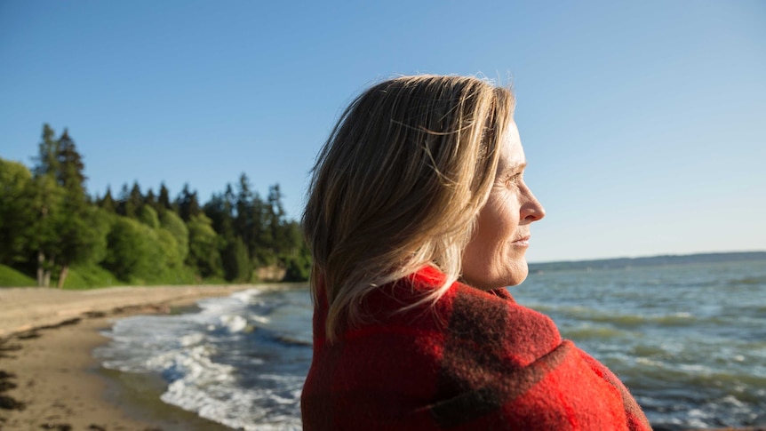 A woman wrapped in a blanket looking at a sunny ocean view.