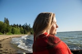 A woman wrapped in a blanket looking at a sunny ocean view.