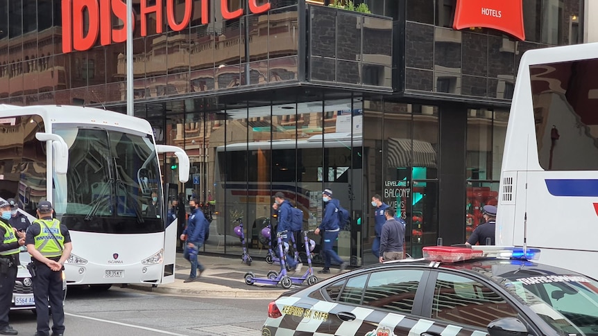 A police car and buses parked outside of a hotel where football players can be seen leaving.