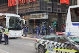 A police car and buses parked outside of a hotel where football players can be seen leaving.