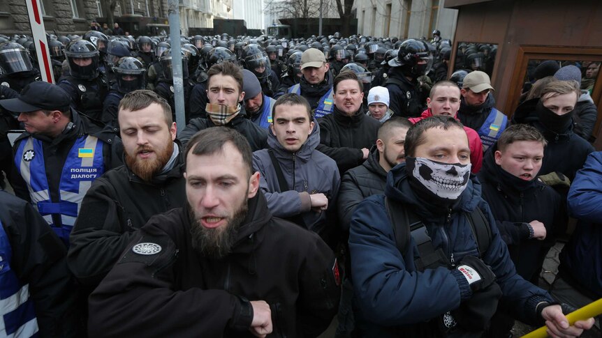 A group of men who are members of Ukraine's National Corps far-right activist group rally, with police behind them.