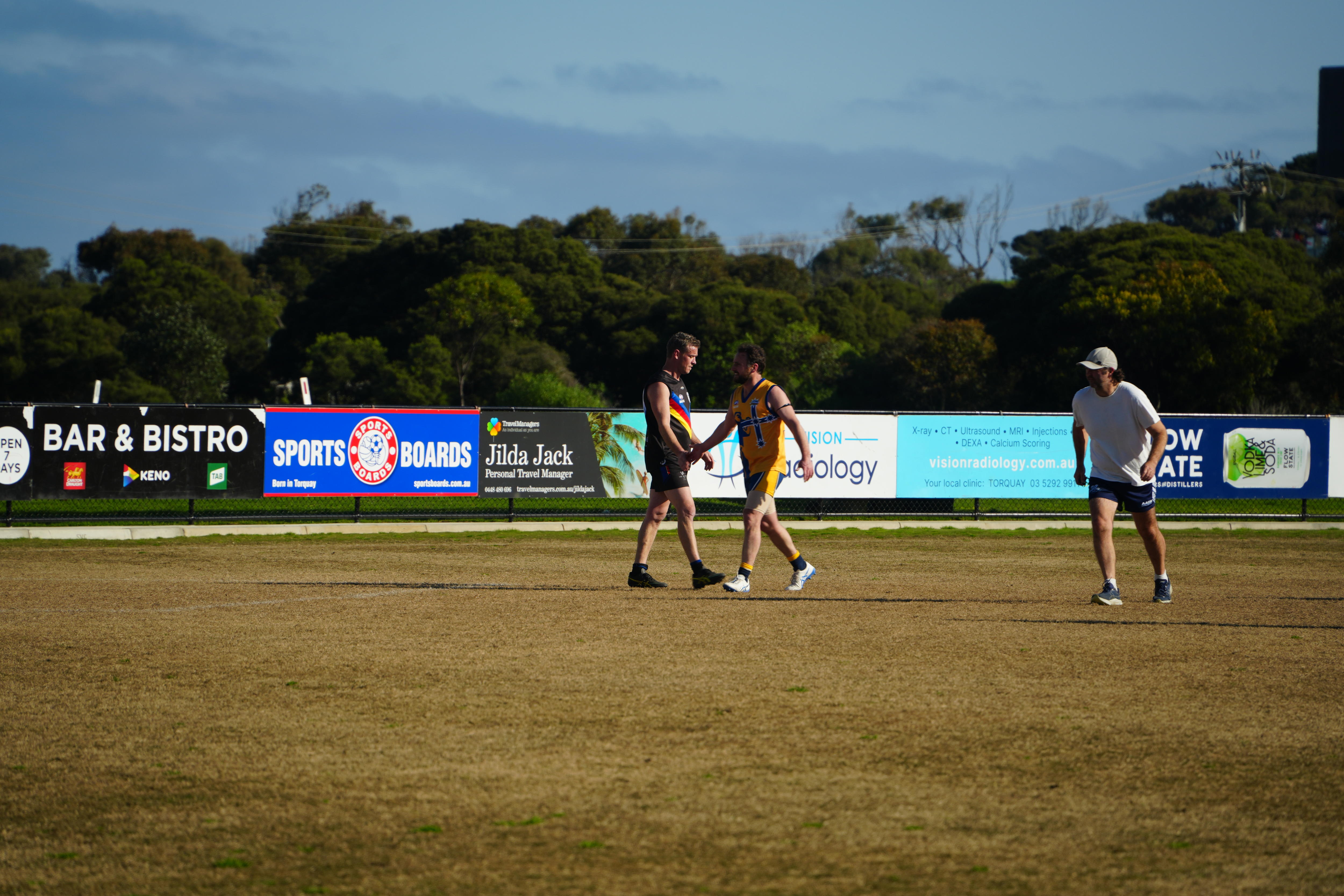 Two players, one from each team, give each other a high five as the walk past each other on the footy field