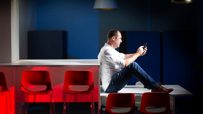 A man sits on a table using his mobile phone with chairs in the foreground.