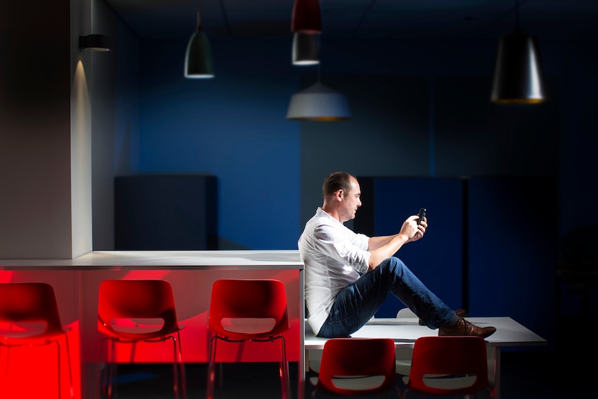 Roger Patulny sits on a table using his mobile phone.