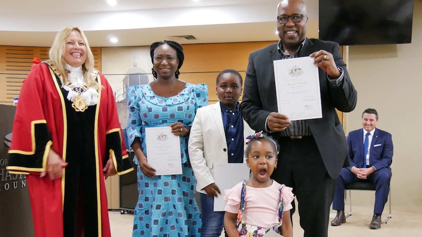 Ngerian family standing with the Mayor holding up their certificate of citizenship smiling with their 8 and 3 year old children.