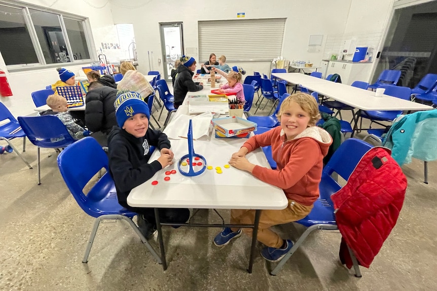 Two children sit smiling at a table.