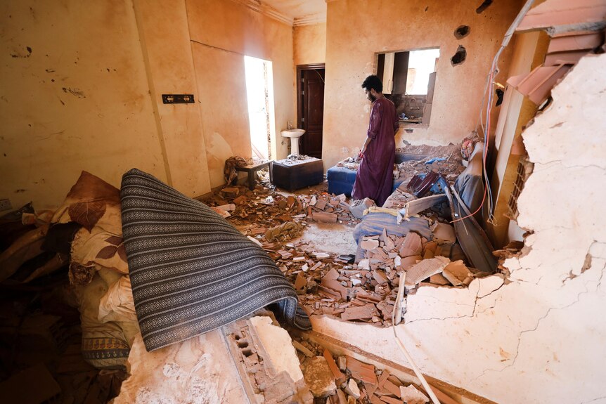 A man walks through the rubble of his home, with crumbling walls and debris