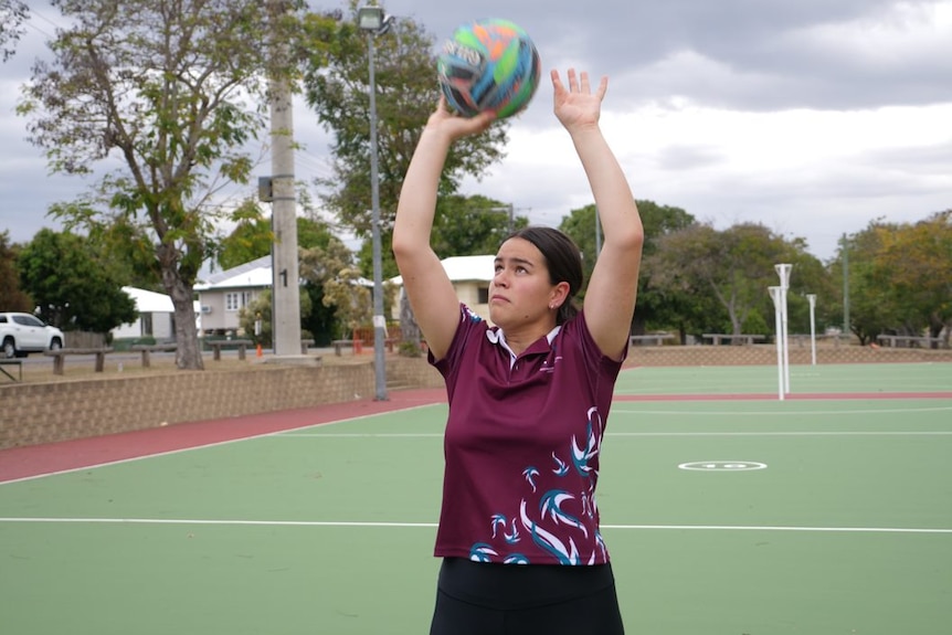Young woman shoots a netball at the hoop.