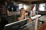 A blonde woman stands behind a bar pouring a glass of beer smiling at the camera.