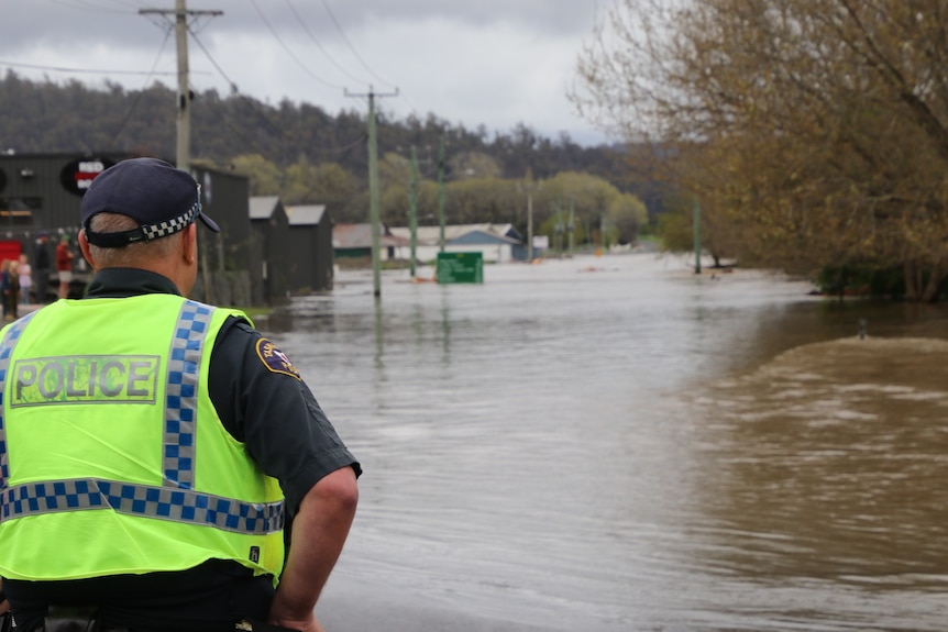 Tasmania Police officer looks at a flooded area near a town.