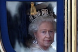 The Queen, wearing a crown and with a pensive expression, looks out of a horse-drawn carriage 