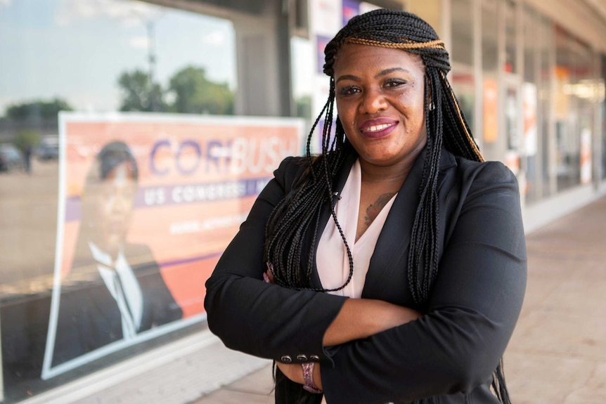 A black woman with black hair smiles with her arms crossed in front of her while wearing a suit.