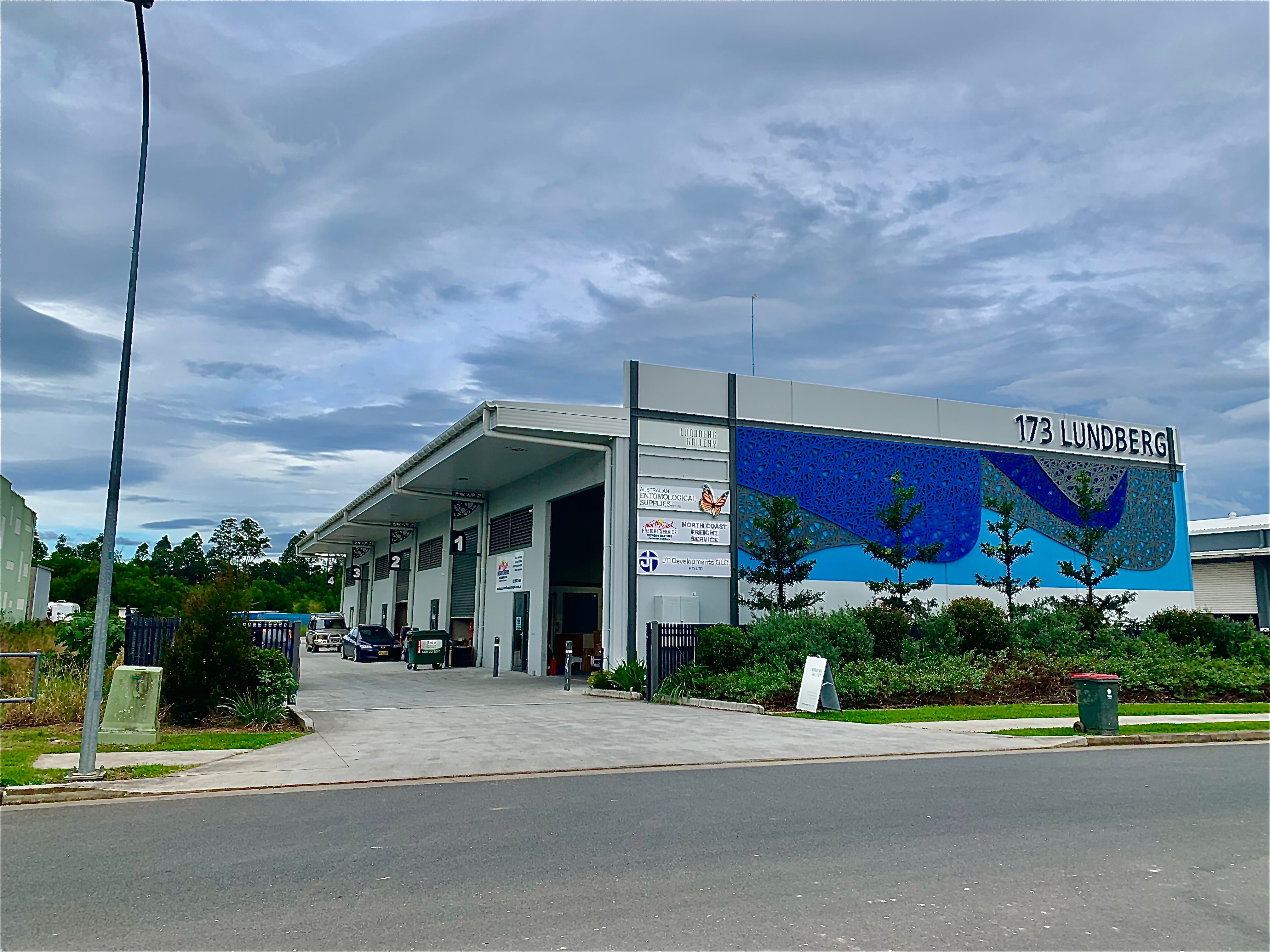 Large concrete industrial estate building with vivid blue mural on wall and cloudy skies 