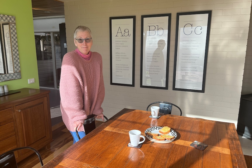 Judith Conway is standing in her home next to a table with two cups of tea and cake sitting on it 