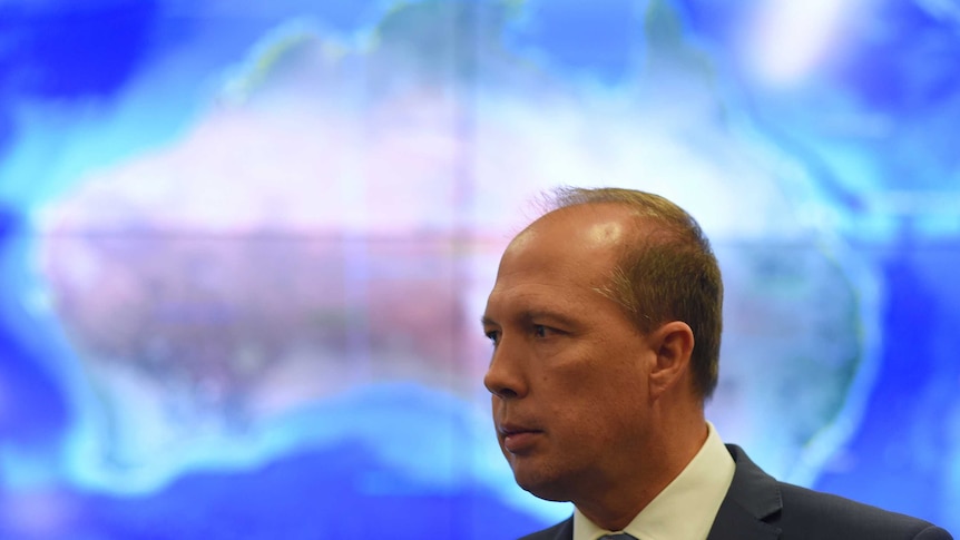 Immigration Minister Peter Dutton stands in front of a lit-up map of Australia.