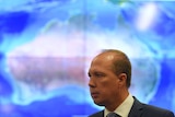 Immigration Minister Peter Dutton stands in front of a lit-up map of Australia.