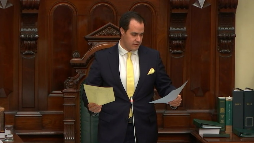 A man in a suit holding a yellow and a white piece of paper