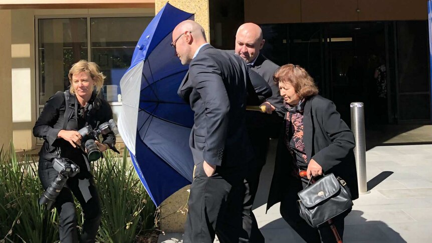 Dragi Stojanovski uses an umbrella to shield his brother and mother from a photographer as they leave the Coroners Court.